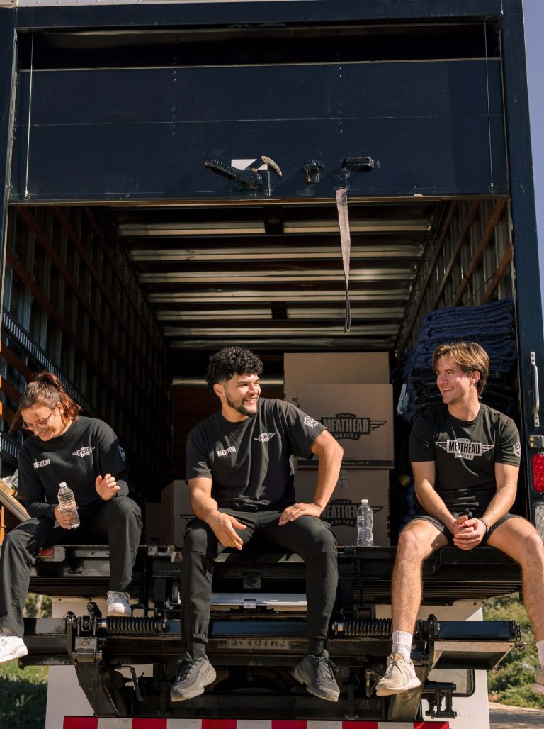 Three Meathead movers sitting on the back of a moving truck