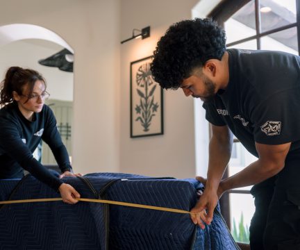 Meathead movers wrapping a dresser in a protective moving blanket