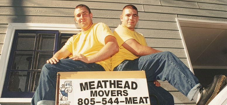 Vintage photo of two young men sitting beside an original Meathead Movers sign