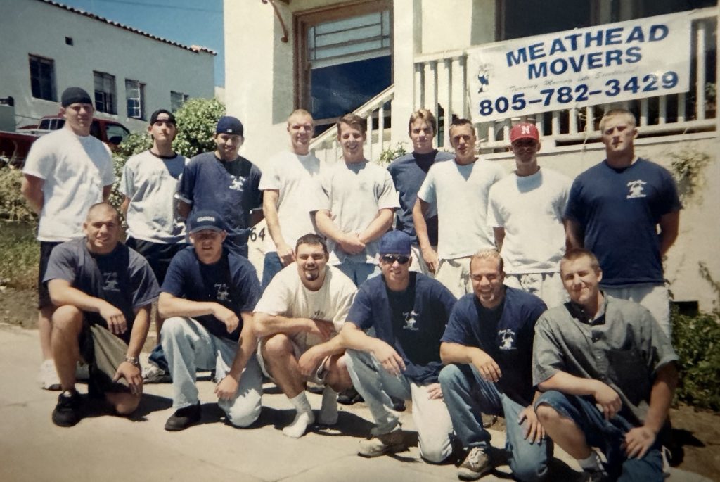 Vintage group photo of the early Meathead Movers crew in front of the company sign