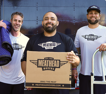 Three Meathead movers holding a moving box and moving blanket beside a truck
