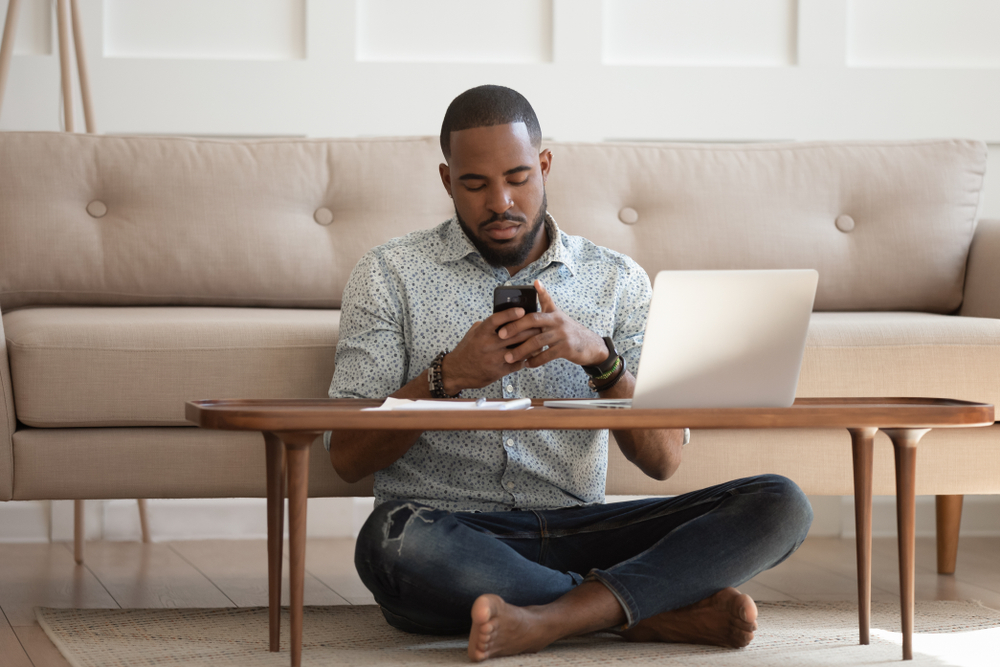 A man sitting on the ground at a desk on his phone.